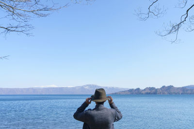 Rear view of man wearing looking at lake against clear sky