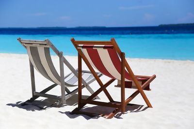 Deck chairs on beach against sky