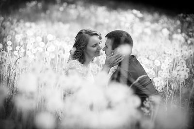 Smiling bride kissing groom while standing by plants