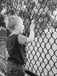 Side view of boy standing by chainlink fence