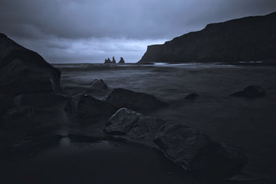 Rocks on beach against sky at dusk