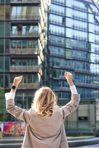 Rear view of woman with arms raised standing against building