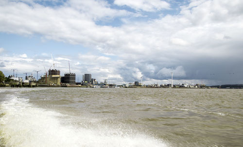 View of buildings by sea against cloudy sky