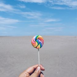 Cropped image of hand holding colorful lollipop at beach against sky