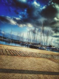 Sailboats moored at harbor against cloudy sky