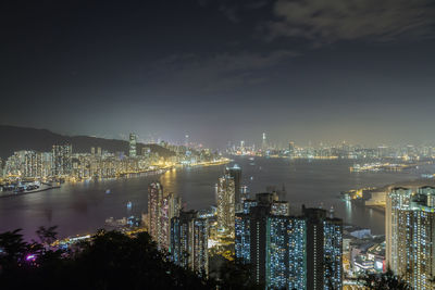 Illuminated cityscape by sea against sky at night