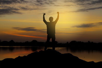 Silhouette man standing by lake against sky during sunset