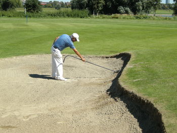 Full length of golfer checking sand trap