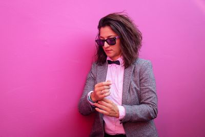 Businesswoman wearing sunglasses while standing against pink wall