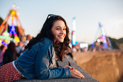 Portrait of smiling woman sitting in city against sky