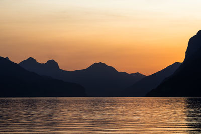 Scenic view of lake by silhouette mountains against sky during sunset