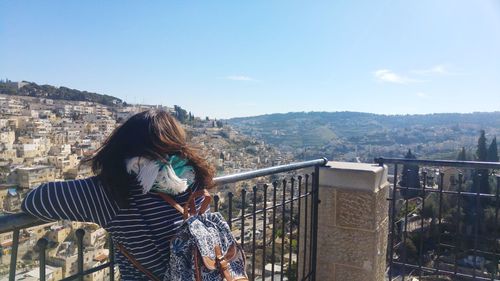 Rear view of woman looking at cityscape from balcony against sky