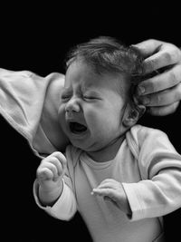 Cropped hand touching crying toddler girl against black background