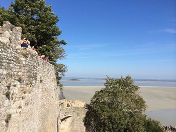 People on cliff by sea against blue sky