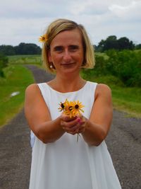 Portrait of woman holding yellow daisies while standing on country road