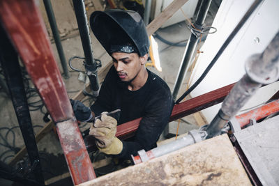 Young male welder wearing welding helmet while working at construction site