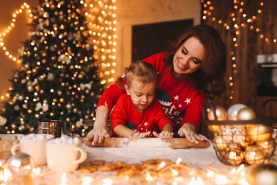 Cheerful parents and a child in red pajamas prepare christmas cookies in the decorated kitchen