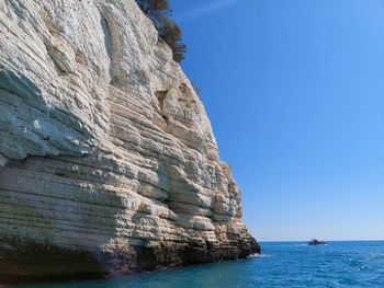 Rock formations in sea against clear blue sky
