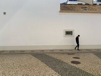 Man walking on footpath against building in city