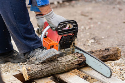 Low section of man cutting wood with chainsaw