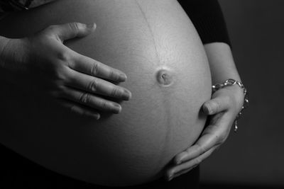 Midsection of pregnant woman touching stomach over black background