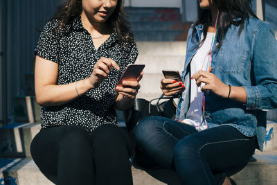 Midsection of female friends using smart phones while sitting on steps