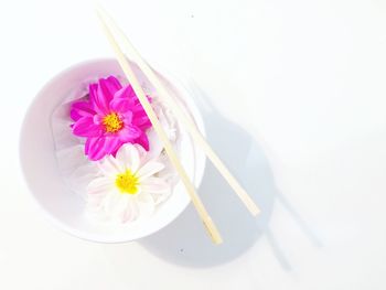 High angle view of chopsticks on bowl with white and pink flowers on table