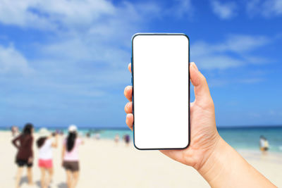 Midsection of person holding smart phone at beach against sky