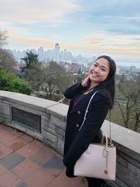 Portrait of smiling young woman standing against cityscape