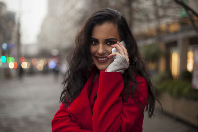 Smiling young woman talking on mobile phone while standing on city street