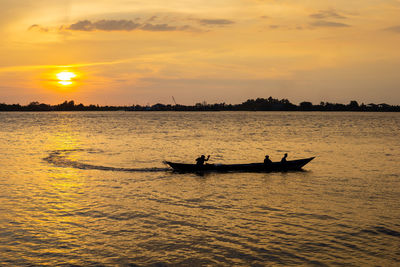 Silhouette people on sea against sky during sunset