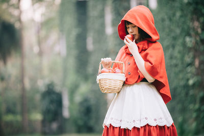 Woman holding hat while standing against plants