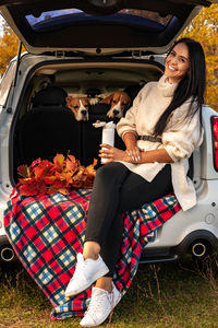 Portrait of smiling woman sitting in car trunk