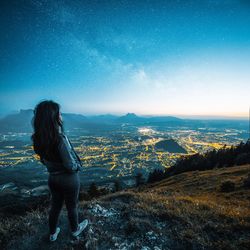 Rear view of woman standing on landscape against sky at night