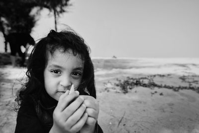 Portrait of cute girl holding seashell at beach against sky