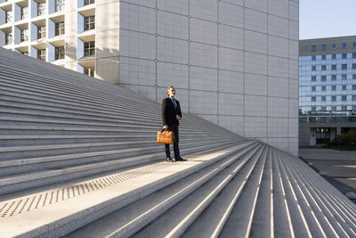 Mature businessman holding bag standing on staircase in front of building