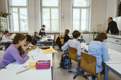 Male and female students studying together while sitting on desk in classroom