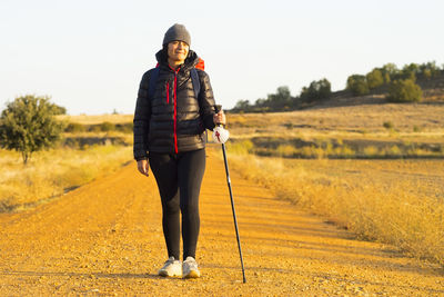 Female hiker walking on field against clear sky