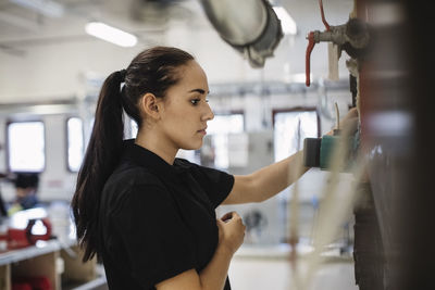 Side view of female auto mechanic student analyzing machinery at workshop