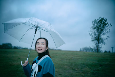 Side view of smiling woman holding umbrella on land