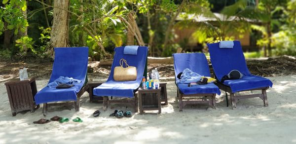 Empty chairs on beach against trees on field
