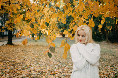 Beautiful blonde woman with autumn leaves on fall nature background. alone brooding woman in white 