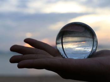 Close-up of hand holding crystal ball against sky