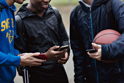 Midsection of friends holding smart phones while standing on basketball court