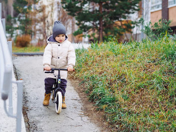 Cute toddler boy in stylish skirt riding on his balance bike at autumn park