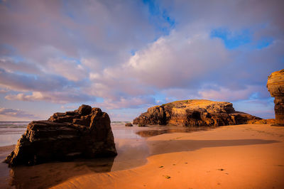 Rock formation on beach against sky during sunset