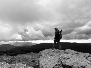 Man standing on rock looking at mountain against sky