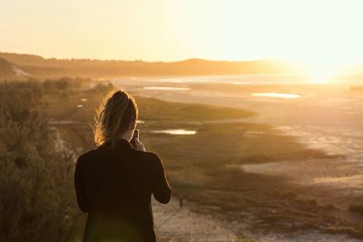 Rear view of woman using mobile phone on field during sunset