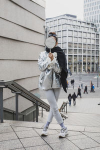 Young woman holding mirror while standing on steps in city