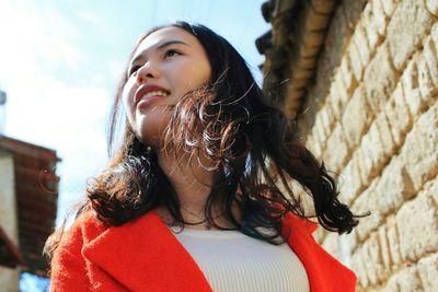 Low angle view of smiling young woman by wall